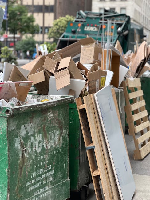 A waste collection worker wearing a high-visibility yellow vest and dark clothing is operating a large, white waste collection vehicle, focusing on the control panel near the rear of the truck. The ve